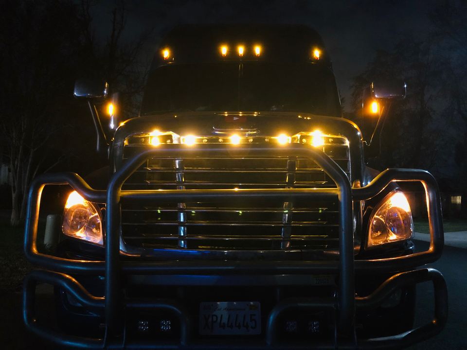 Front of a semi-truck at night with amber LED lights on the grille and visor